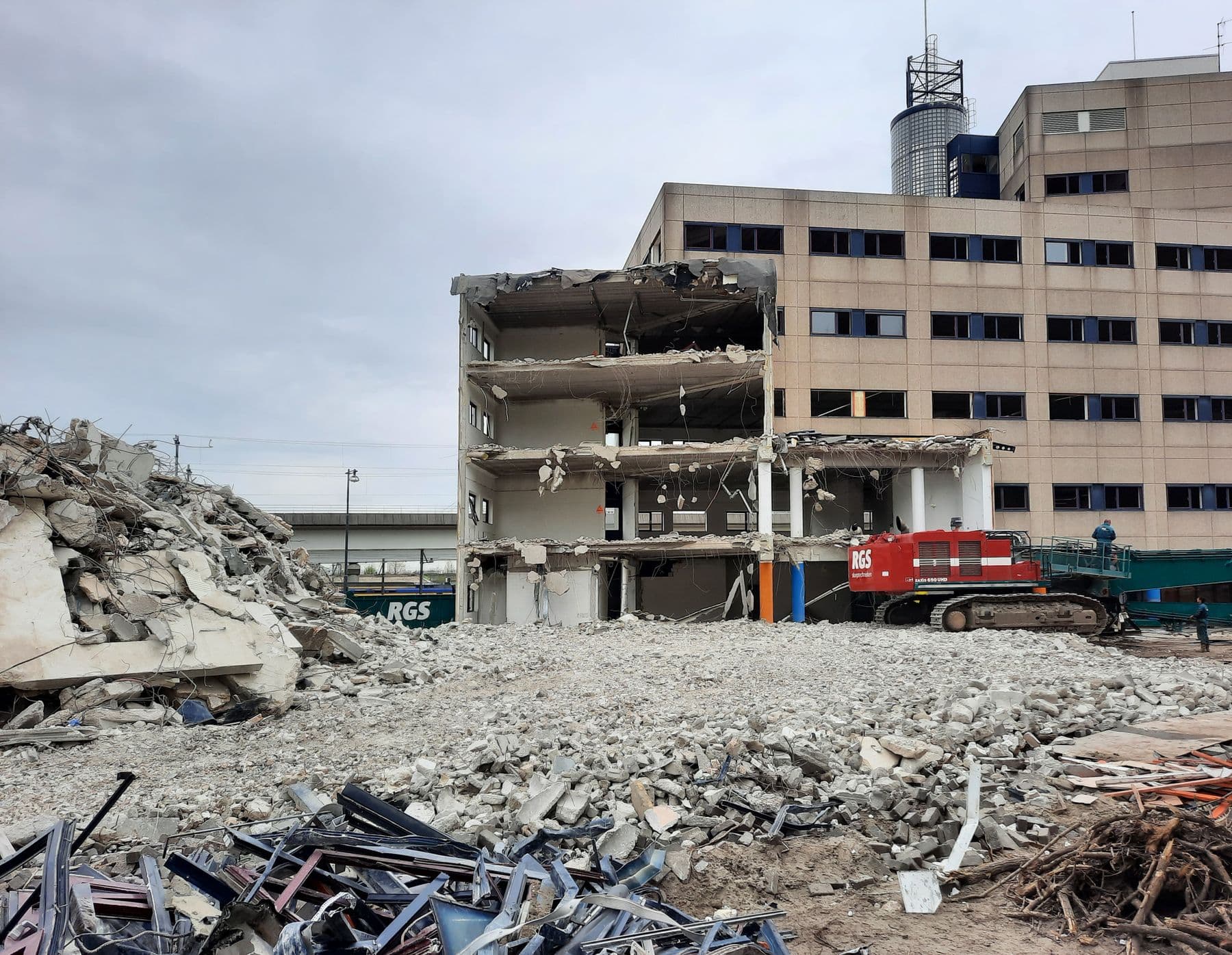A large concrete building partly torn down, with a field of crushed concrete and twisted rebar in front of it.