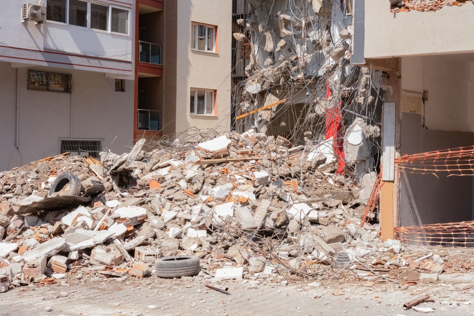 A heap of broken brick and concrete beside an apartment building that is partly demolished.